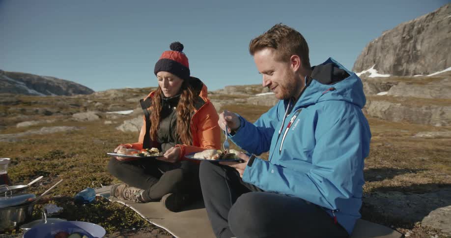 Man and woman sitting and eating on a desolate mountain