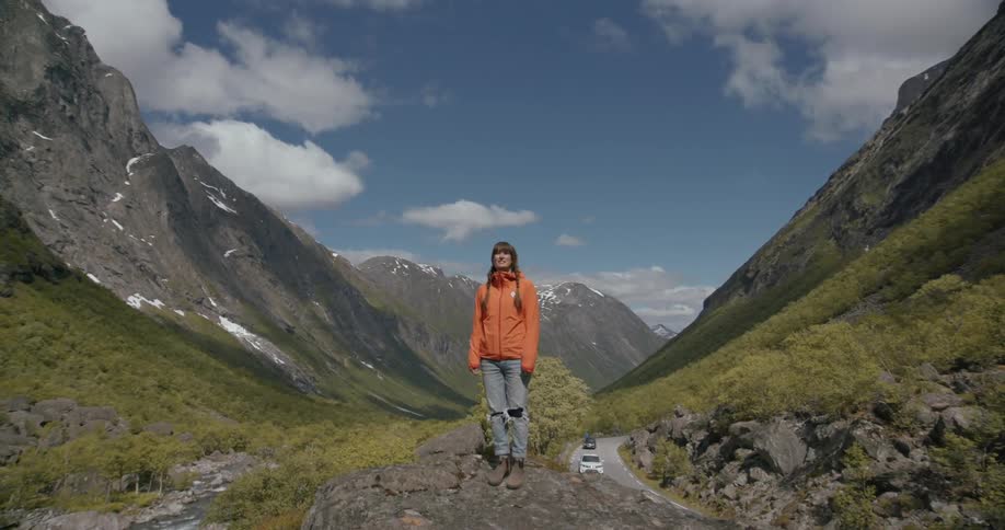 A man is standing on a cliff as cars drive below
