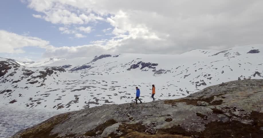 Two people walking towards the edge of hill overlooking snow covered mountains
