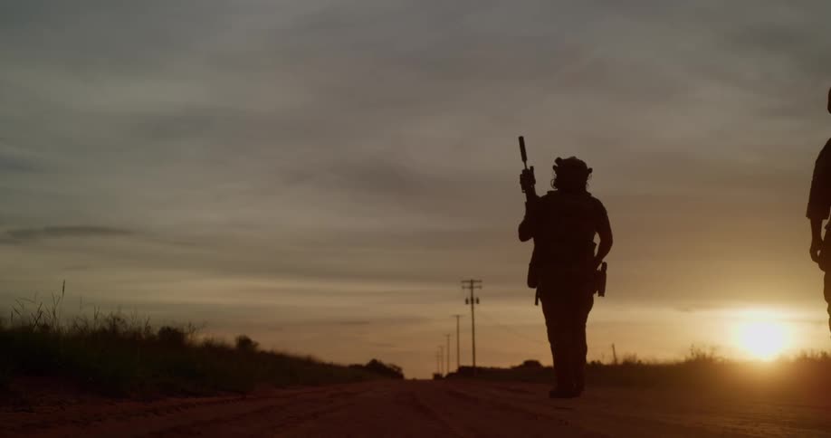 Armed men walk down deserted road at sunset