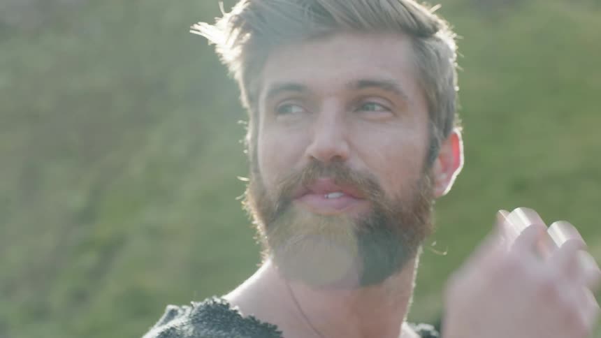 A bearded man stands outdoors in direct sunlight while scanning his surroundings