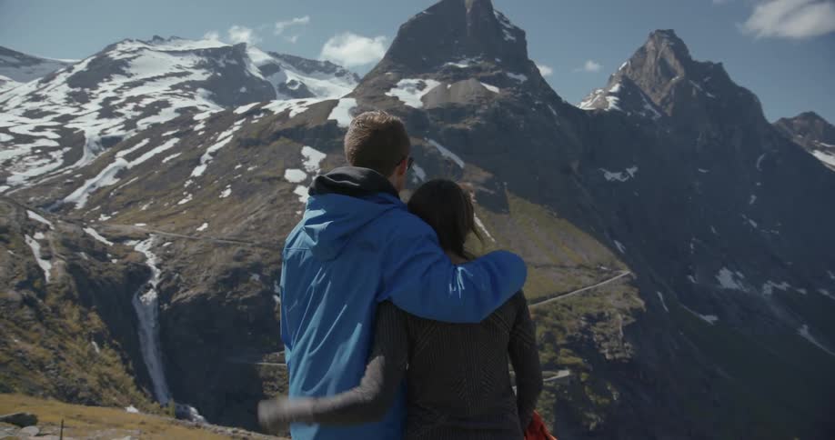 A man and woman embrace overlooking a view from a mountain top