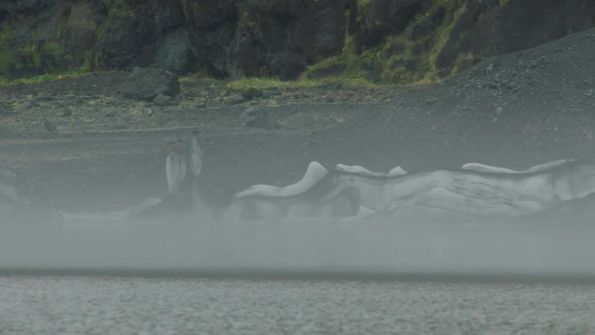 A coast with water and ice with a cliff in the background