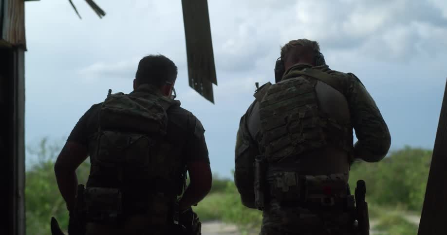 A soldier with his gun pulled stops another soldier from walking forwards and then he slowly moves ahead
