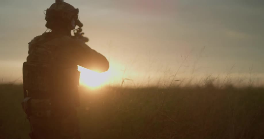 A soldier with a helmet and a rifle walking on a grassy field with the sky and clouds in the background
