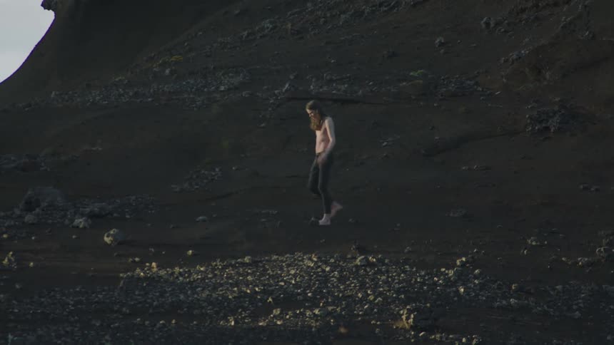A man walking on dirt with a cliff the sky and clouds in the background
