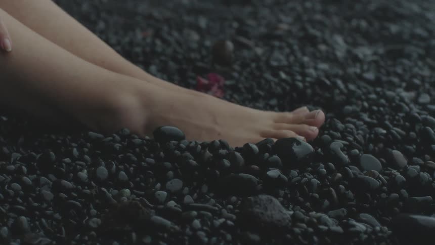 Bare legs and feet on black rocks and a hand resting on the leg