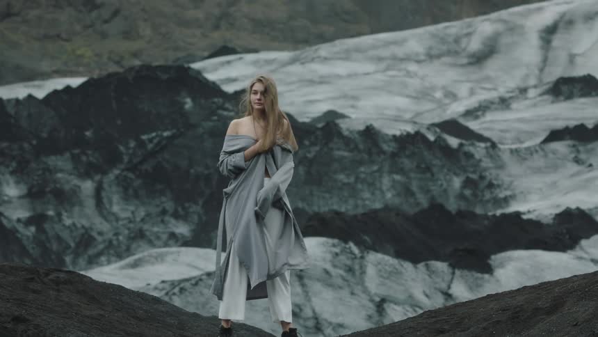 A woman running on a rocky cliff holds on to her jacket and reveals her bare shoulders