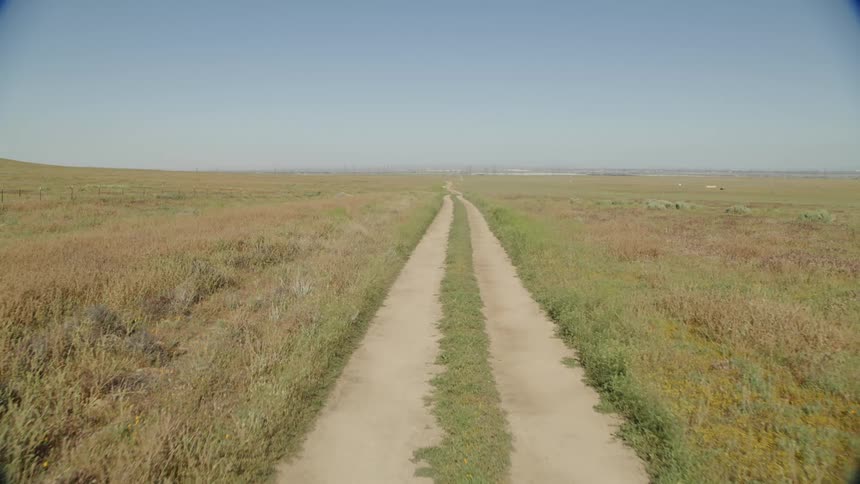 A dirt path on a grassy field with the sky and clouds in the background