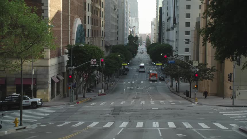 A city street with buildings vehicles trees and traffic lights with the sky and clouds in the background