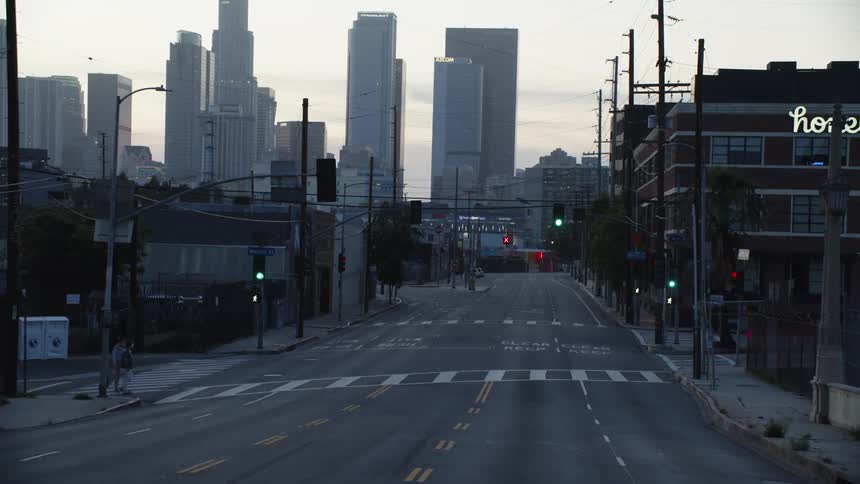 Two pedestrians wait to cross a quiet street and a vehicle drives on the street in the distance