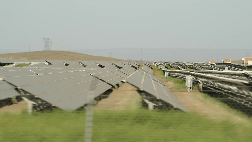 Camera shows a field with hills full of solar panels absorbing the sun around midday
