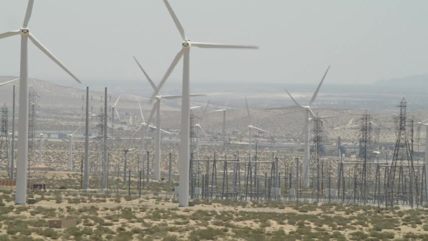 Spinning wind turbines surround a group of transmission towers in a vast grassland on a foggy day