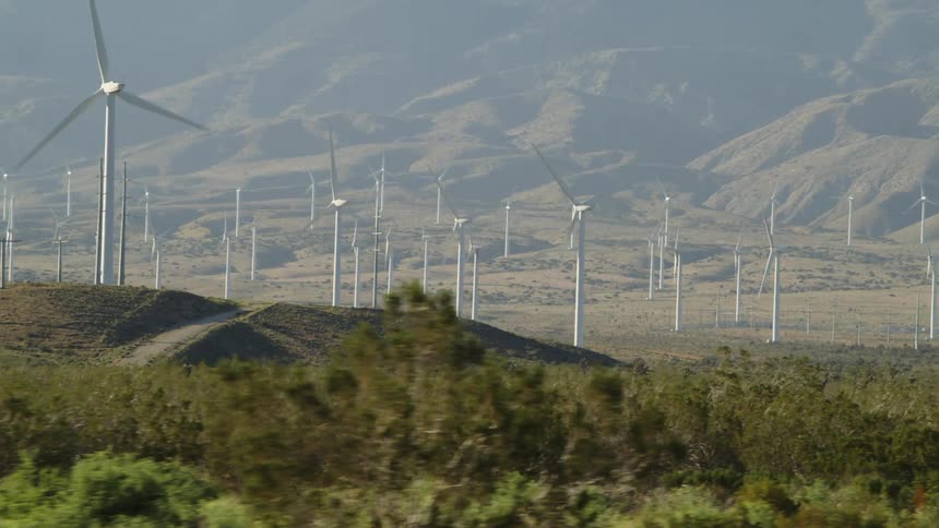 Wind turbines spinning on a wind farm in the hills next to the mountains