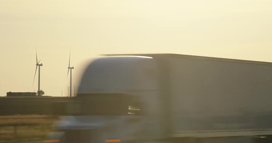 A highway with trucks and a row of wind turbines with grass in the middle