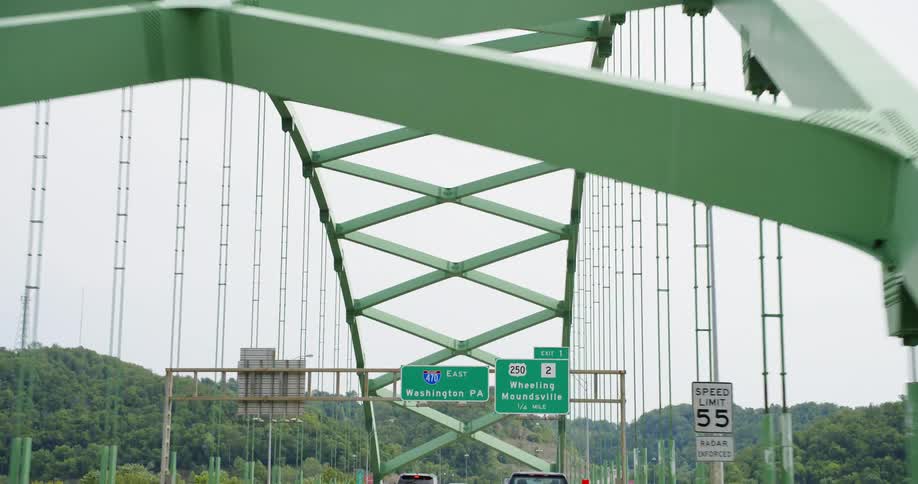 Vehicles driving on a bridge with signs with the sky and clouds in the background