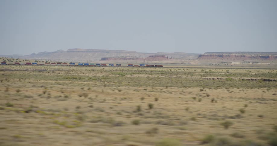 A grassy plain with a train with a canyon the sky and clouds in the background