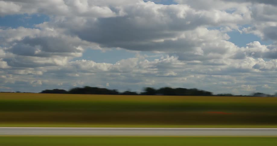 Time lapse of passing grass fields under the white clouds in the blue sky
