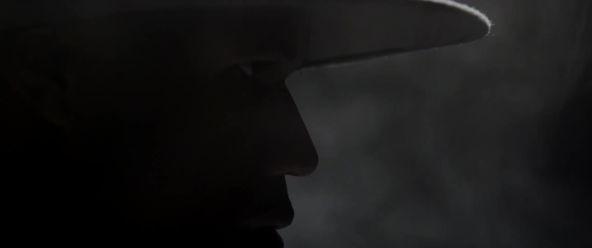 The silhouette of a man wearing a hat can be seen in a darkened room