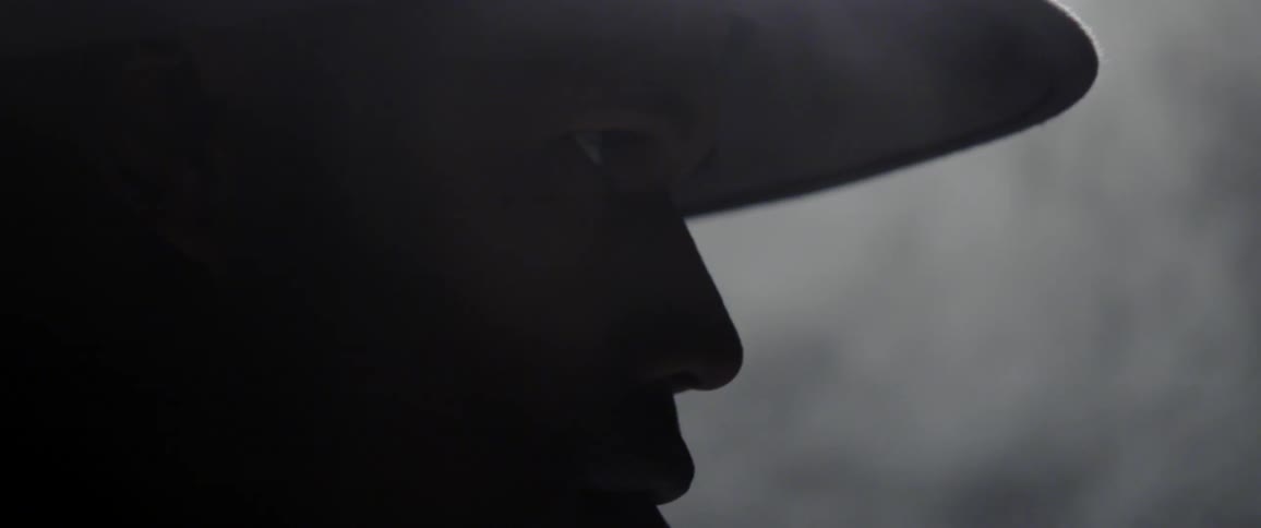 The silhouette of a man wearing a hat can be seen while smoke swirls behind him