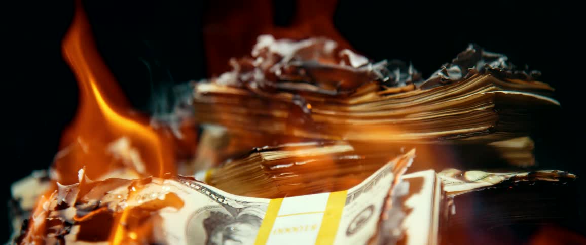 Several stacks of one hundred dollar bills are engulfed in flames as they burn