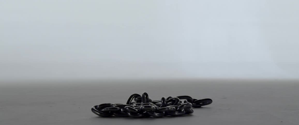 A medium length black chain is abruptly dropped from above and lands on a flat surface