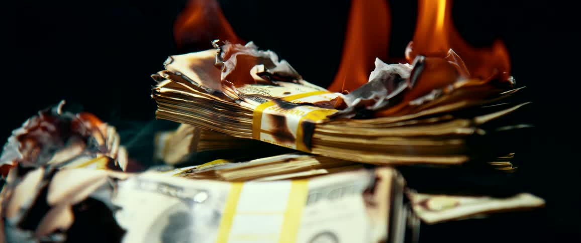 A stack of money burning with fire and smoke with a black background
