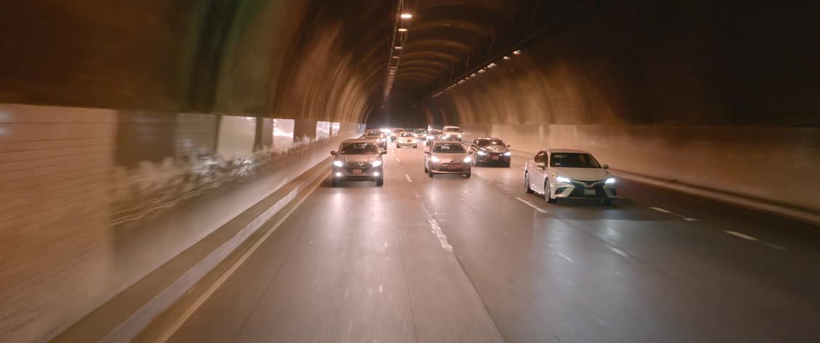Vehicles with headlights on driving on the four lanes inside a tunnel
