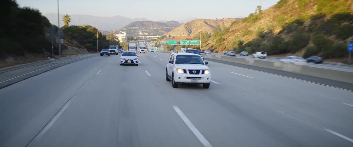 Vehicles driving on a highway with signs with hills the sky and clouds in the background