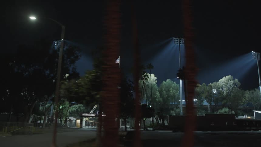 A stadium with spotlights and a flag with trees and a parking lot in the foreground
