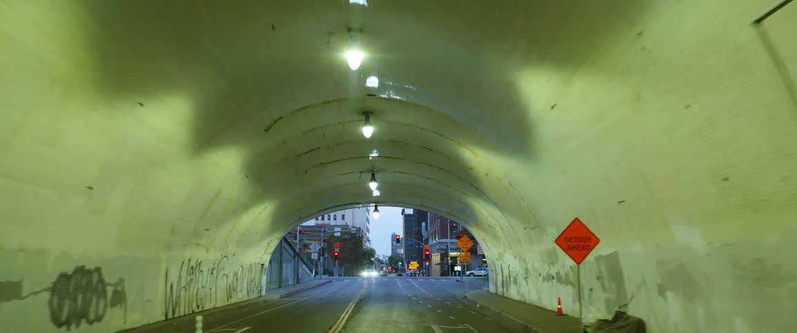 Interior of a tunnel that opens to a city intersection with traffic and pedestrians