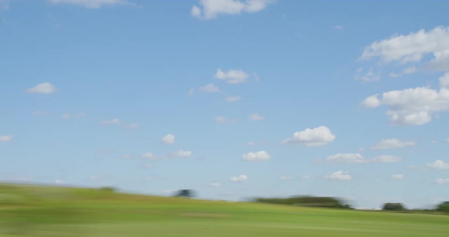 Time lapse of passing green pastures under blue sky dotted with clouds