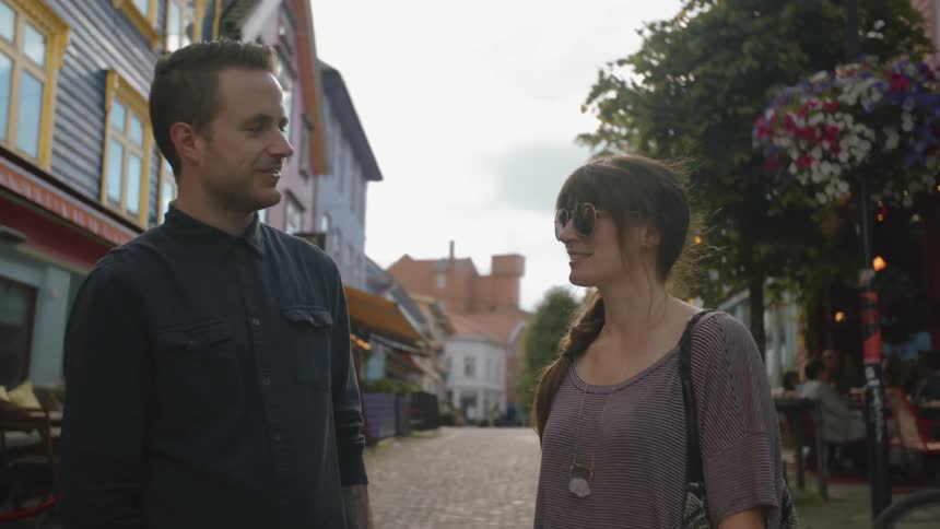 A man and women stand on a street and talk