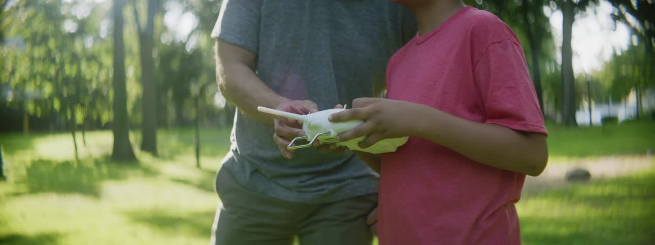 A man and boy play with a toy while standing outdoors surrounded by grass and trees