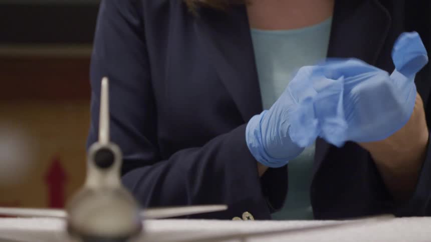 A woman putting on gloves to touch a model plane