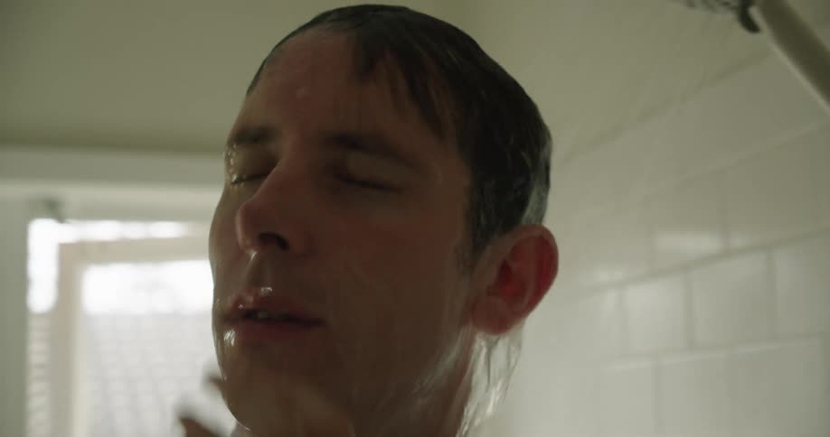 A man is showering in a bathroom with white table and an opened window