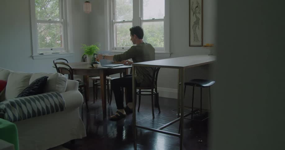 Man sits at the kitchen table opening a laptop working from home