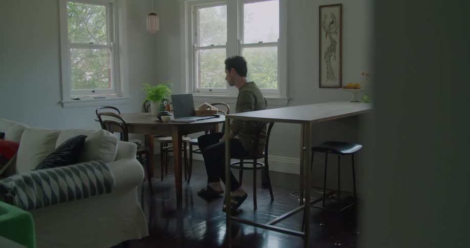 A man in a room walking up and sitting on a chair then opening a laptop