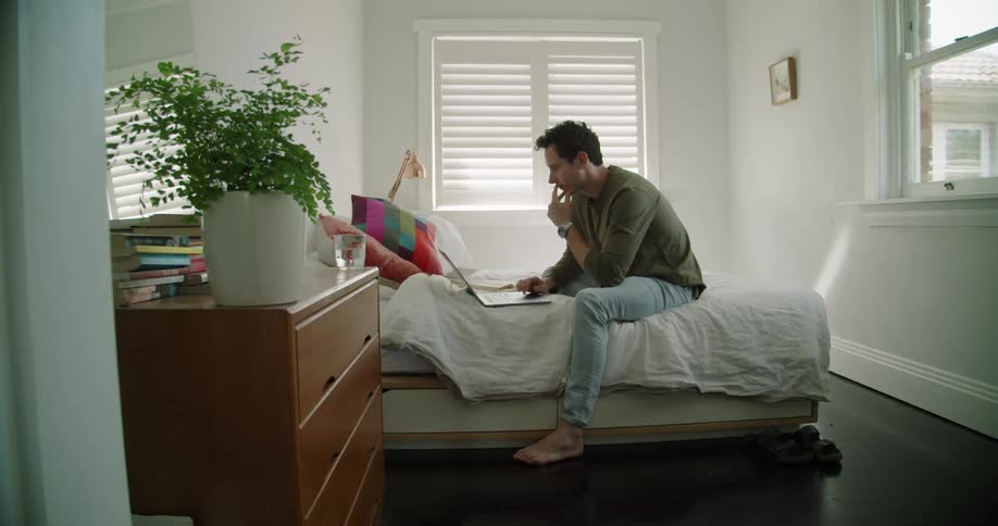 A man sitting on a bed using a laptop