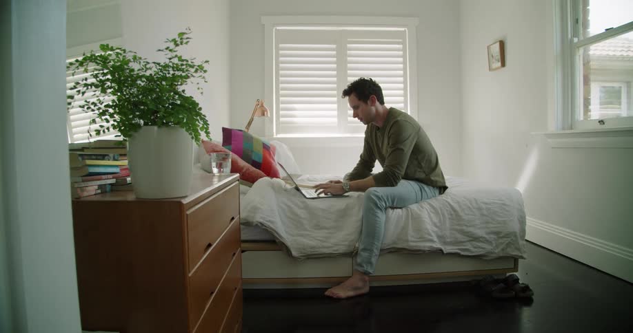 A man is typing on his laptop in bed