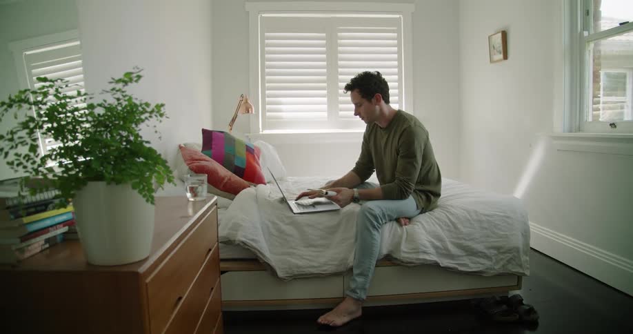 Man typing on laptop while looking through book