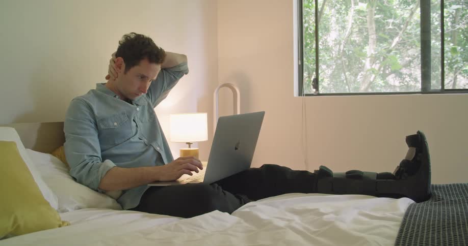 A man with a broken foot working on a laptop