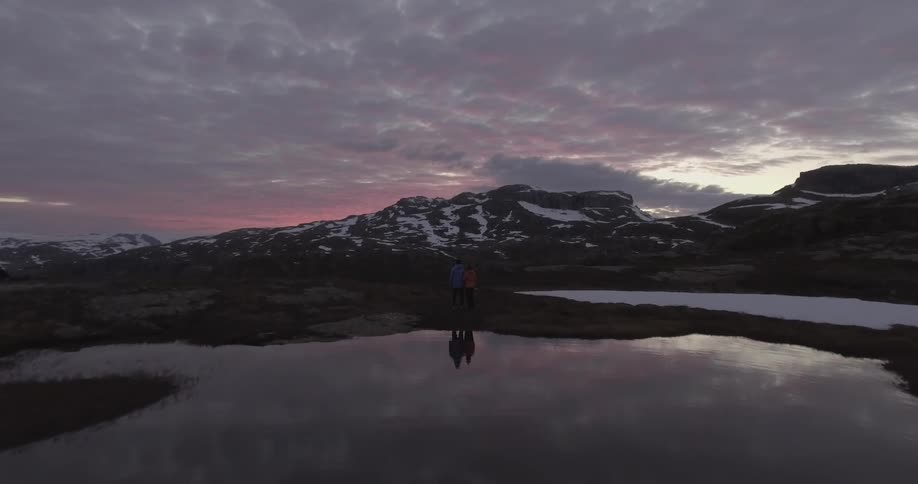 Two people stand near a lake at sunset