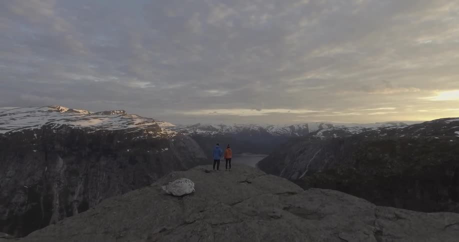 Two hikers stand on a ledge overlooking a mountain range