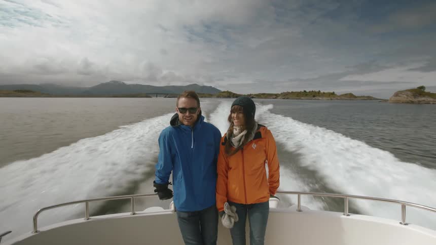 A man and women are leaning against the edge of a boat as it sails
