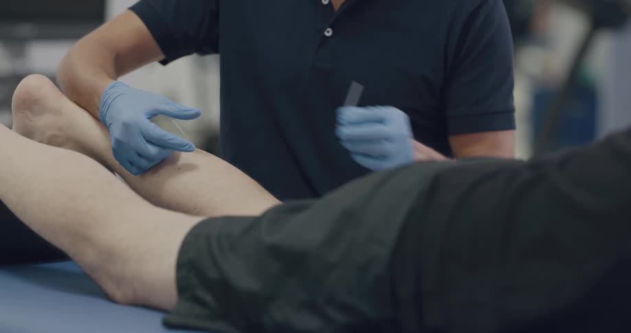 A man in a physical therapy facility gives a person an injection in their leg