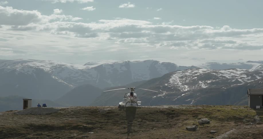Helicopter sitting on a hill overlooking snow covered mountains