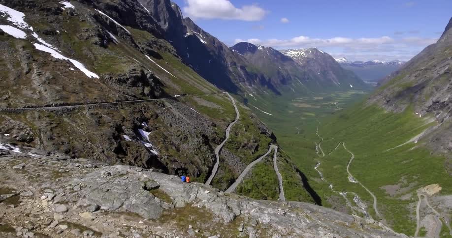 Two people sitting on a rocky cliff looking out at a winding road