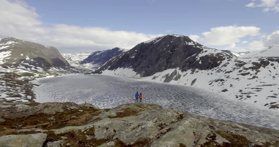Two people enjoying the view of frozen lake surrounded by snowy mountains