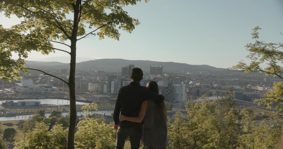 A man and woman have their arms around each other as they look at a city in the distance